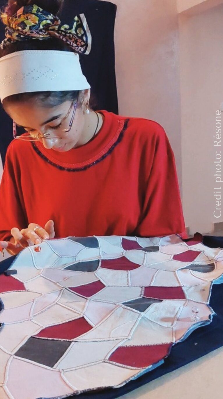 Une artisane en haut rouge assemble à la main un patchwork géométrique.