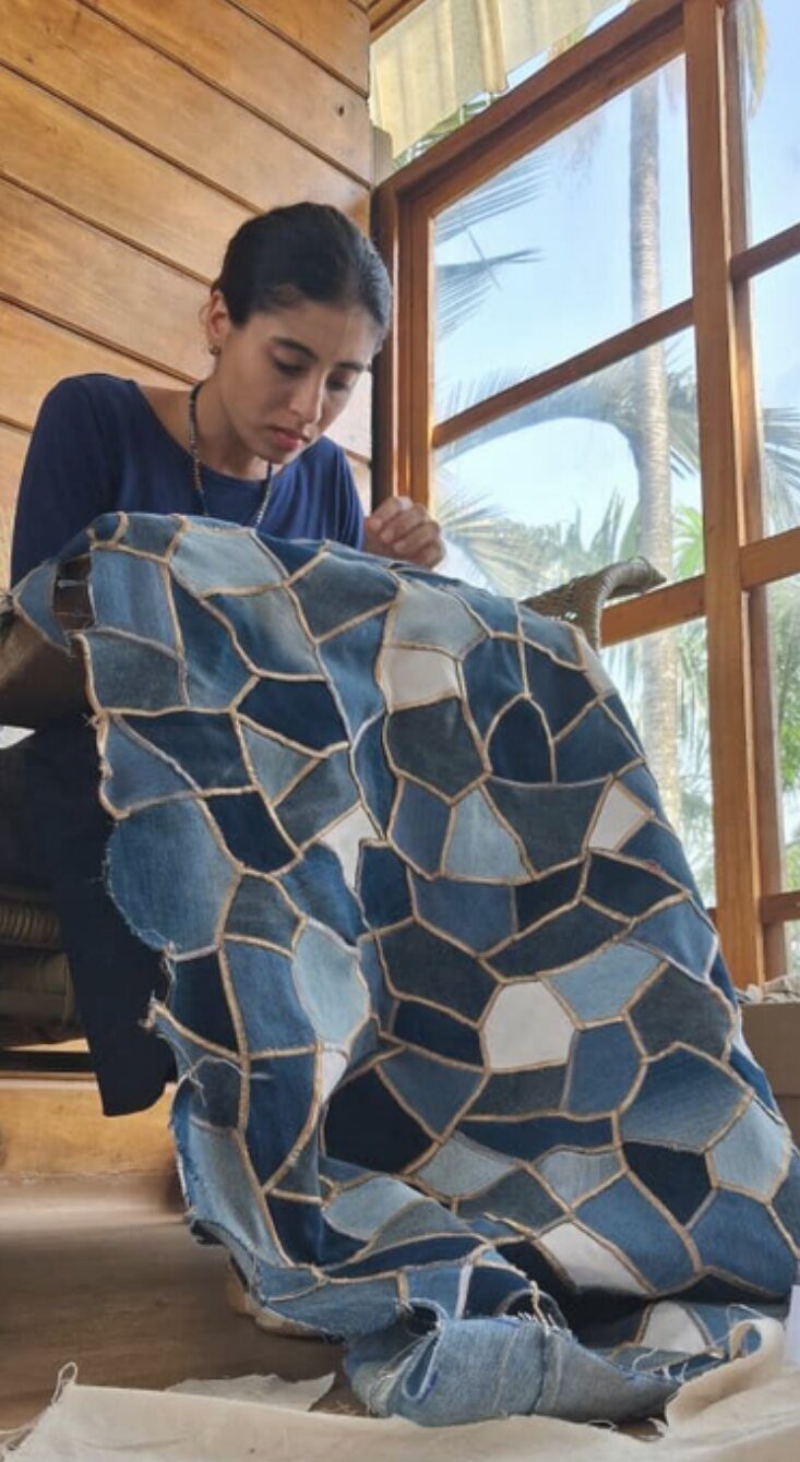 Une artisane déploie la mosaïque en jeans pour en montrer l'envers.